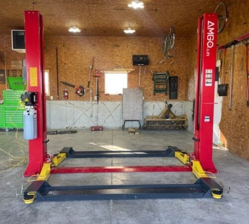 An AMGO 20805 Golf Lift Accessory Kit shown installed on a red two-post lift within a garage, with the platforms spanning the width to lift a golf cart.