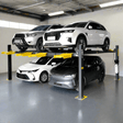 A black AMGO 409-DP Double Parking Lift, with two white SUVs and a dark sedan elevated, showcasing its 9,000 lbs total capacity in a garage setting.