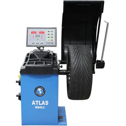 A front view of the blue Atlas WB49-2-PRO Wheel Balancer with a tire mounted on the 40mm shaft, showing the raised LED display and an included measuring caliper.