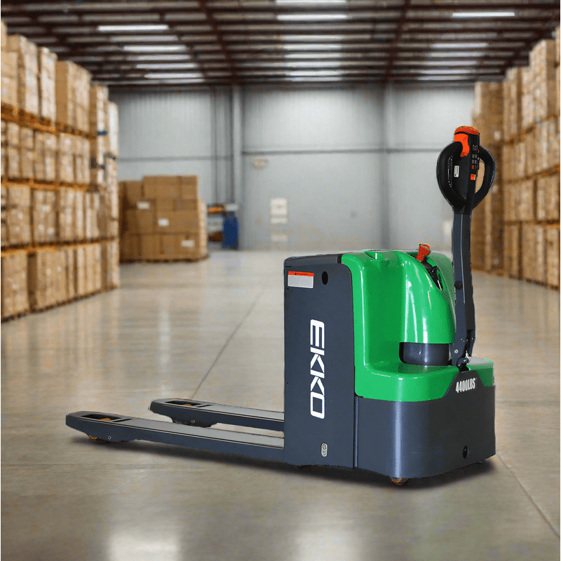 An EKKO EP20E-Li Electric Walkie Pallet Jack with a 4400-pound load capacity sits in the center of a warehouse aisle surrounded by cardboard boxes stacked on pallets.
