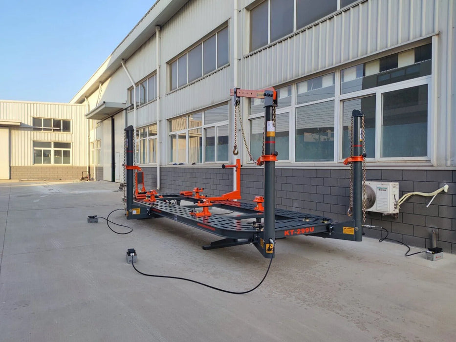 A wide shot of the Katool KT-299U Frame Machine positioned outside of a building, highlighting its full size and portable capabilities. The orange pulling towers and black frame are clearly visible.