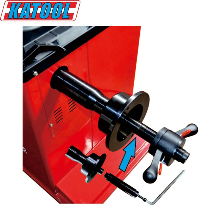 A close-up of a red KATOOL machine with a black spindle and handle, used for tire service. The KATOOL logo is visible in the corner, and a blue arrow points to a part of the machine.