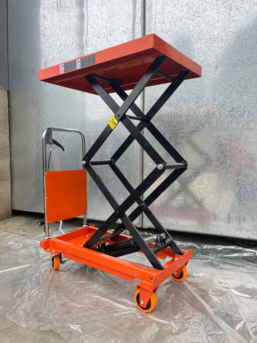 A side view of the Katool Scissor Lift Table, showcasing its folded state with the scissor mechanism fully lowered. The table is made of powder-coated steel and has an orange handle for easy portability.