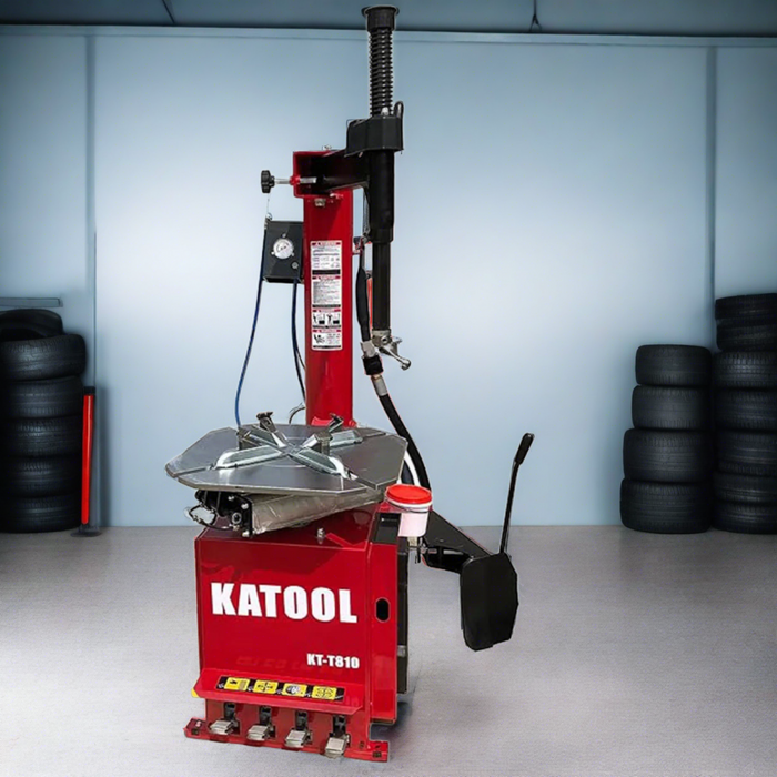 A red Katool KT-T810 tire changer in a workshop, surrounded by stacks of tires, ready for use.