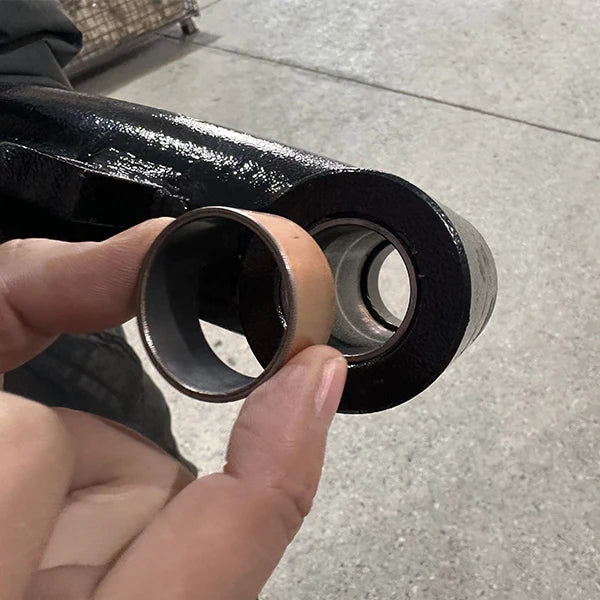 A close-up of a person's hand holding a bronze bushing next to its housing on a black component of the Katool KT-T830 tire changer, highlighting the durable internal part.
