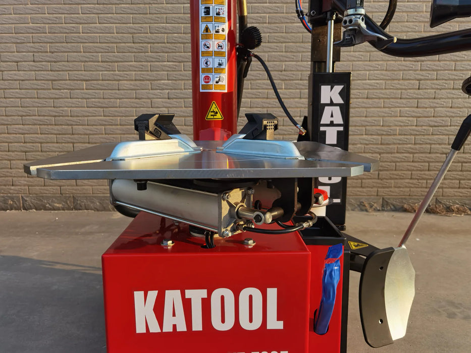 A close-up, angled view of the turntable and lower body of the red Katool KT-T835 tire changer. The silver clamping jaws are visible on the turntable, and the Katool logo is prominent on the machine's base.