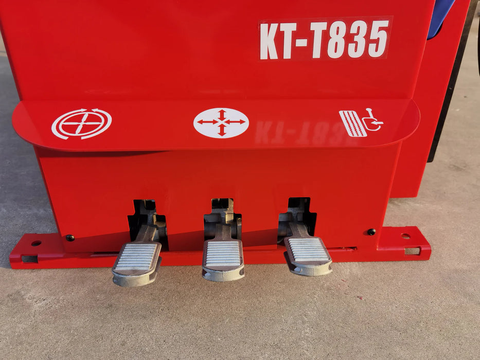 A close-up view of the three silver pedals and the red body of the Katool KT-T835 tire changer. The pedals are clearly labeled with icons for clamping, de-clamping, and rotation, and the machine name is visible.