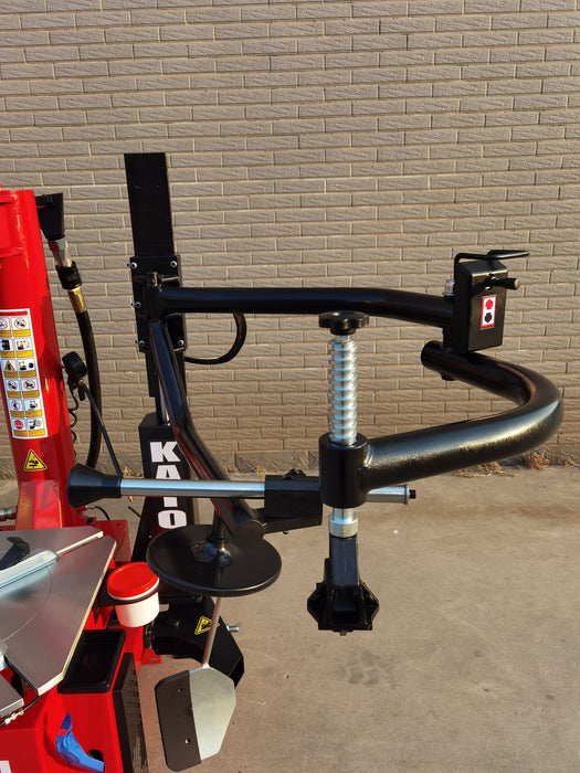 A close-up side view of the black assist arm on the Katool KT-T835 tire changer, highlighting the spring mechanism and the bead seater tool. The red machine body is partially visible.