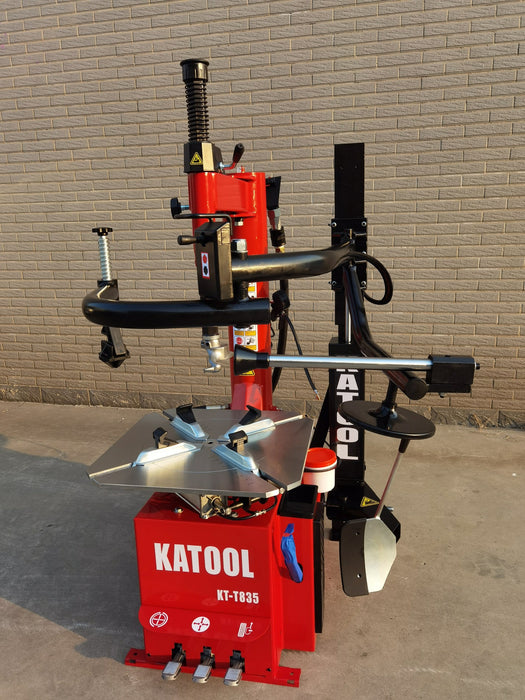 A full-body, three-quarter view of the red Katool KT-T835 tire changer. The double-sided assist arm is fully extended, showing the machine's full operational range.