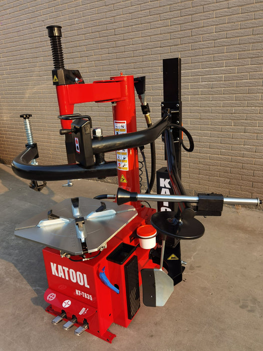 A full view of the red Katool KT-T835 tire changer, with both the bead breaker and assist arm fully extended. The image shows the complete machine and its full range of motion.