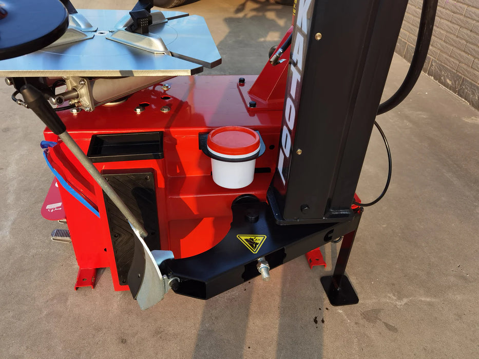 A close-up, ground-level view of the red body of the Katool KT-T835 tire changer. The side-mounted bead breaker is visible with its large silver lever, along with a tool tray on the side.