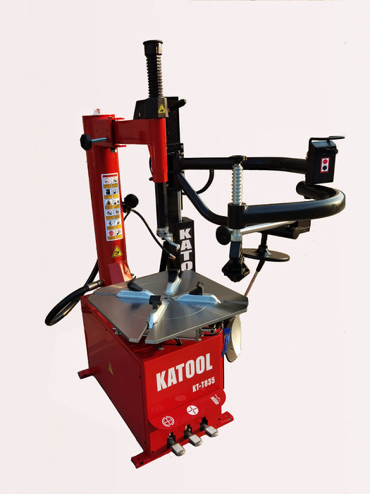 A full view of the red Katool KT-T835 tire changer, showing its compact, closed body design from an angled perspective. The machine is set against a black background, highlighting its professional look.