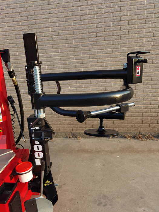 A detailed, angled shot of the Katool KT-T835 tire changer's assist arm, bead seater, and pneumatic controls, with the black and red components visible against a brick wall background.