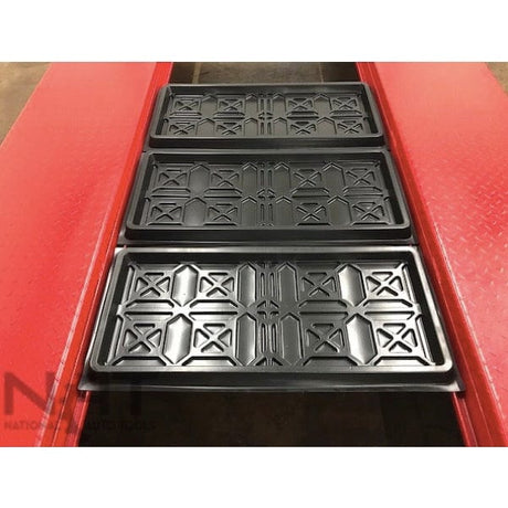 A top-down view of the black rolling drip trays sitting in the runways of the red Triumph NOS9000 four-post lift.