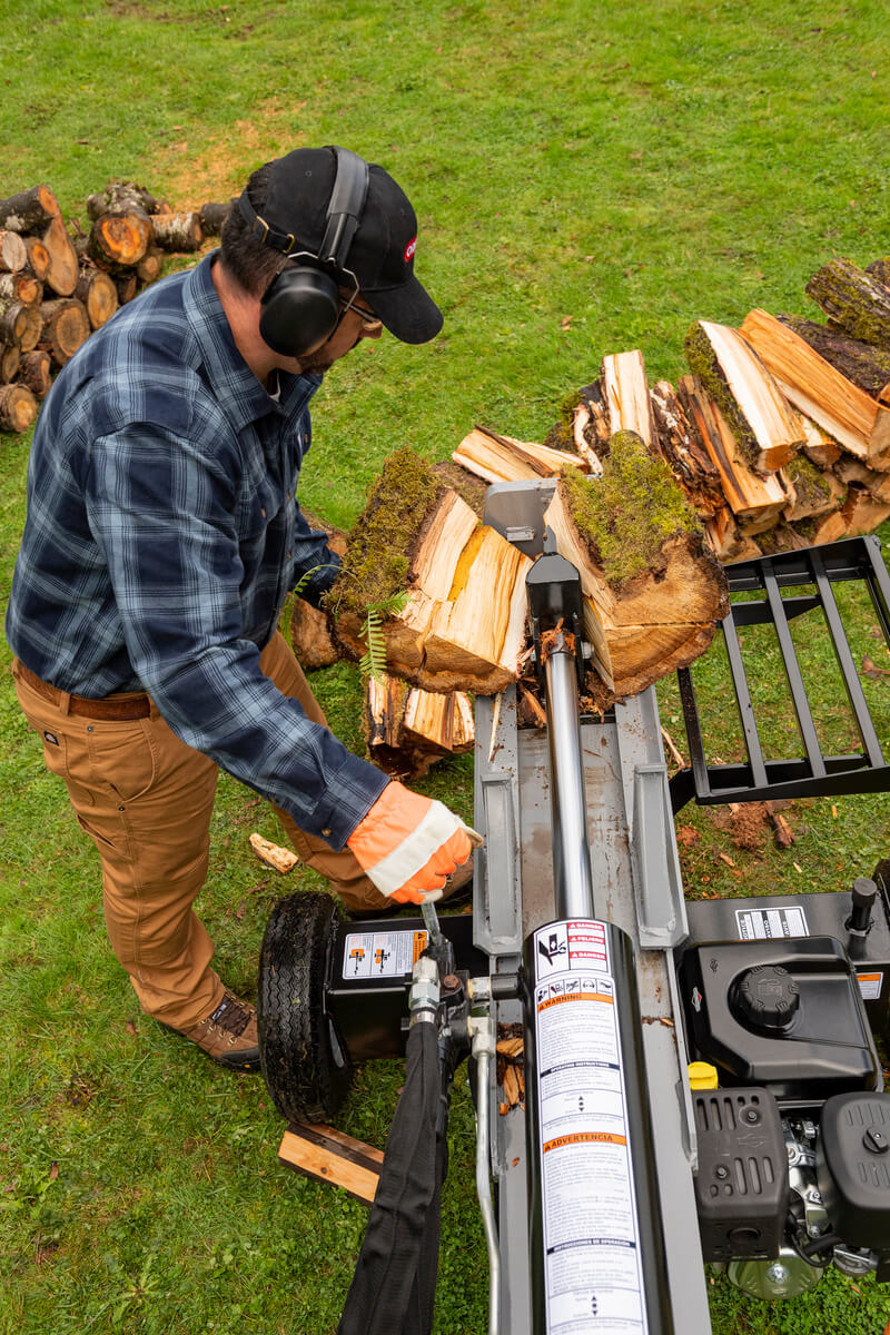 A person operating the Oregon 2500 Series 25-ton log splitter in the horizontal position, splitting logs in a grassy outdoor area.