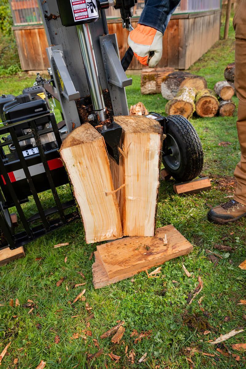 A thick, freshly cut log being vertically split by the gray Oregon 3500 Series 35-ton log splitter in a grassy area.