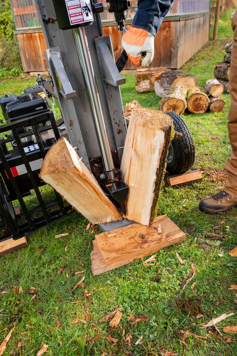 A log being vertically split in half by the gray Oregon 3000 Series 30-ton log splitter in a grassy area with a wooden structure in the background.