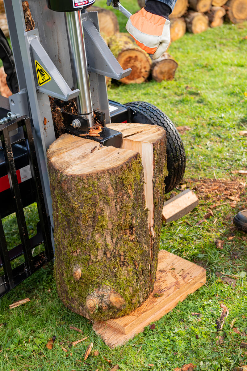 A large mossy log is being vertically split by the gray Oregon 2500 Series 25-ton log splitter on a splitting platform.