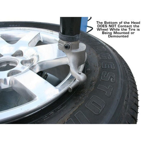 
A close-up view of the mount/demount head on the Atlas TC229LH Rim Clamp Tire Changer with a wheel and tire, showing the note that the head should not contact the wheel while the tire is being mounted or demounted.