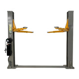 A front view of the Triumph NT-9 Two-Post Auto Lift in a grey color, with its lift arms in the raised position. The power unit is visible on the right post, and a black hose runs between the two posts along the floor.