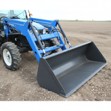 A blue New Holland tractor equipped with a 72" HMG material grapple, standing in a large, open field under a cloudy sky.